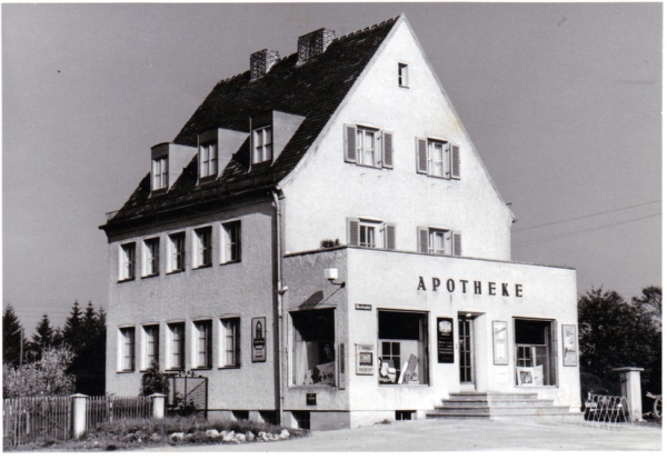 Die historische Rosen-Apotheke Olching, ein freistehendes weißes Haus mit der Aufschrift APOTHEKE.